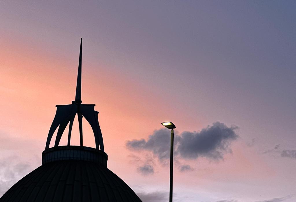 Silhouette of a dome with a pointed spire against a colorful sunset sky featuring soft clouds.